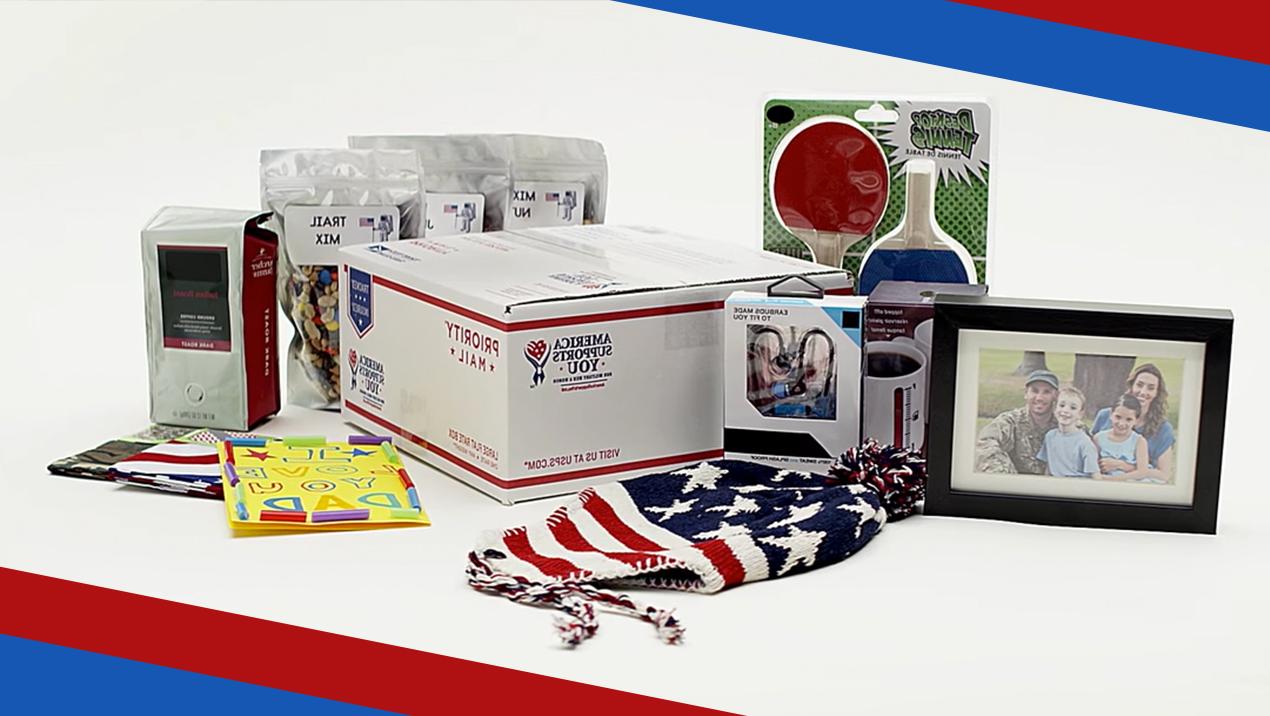  A Priority Mail box surrounded by items that can be shipped inside it including a family photo, a hat designed to look like an american flag, game paddles, birthday cards, trail mix, coffee, and small electronics.